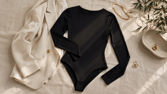 Opaque black long-sleeve bodysuit arranged with a cream tailored blazer and minimal gold accessories