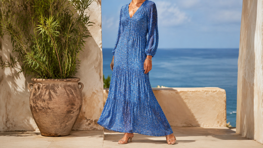 Woman wearing a flowing azure-blue printed maxi dress in a sunlit coastal courtyard