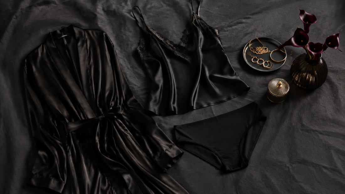 Black satin camisole, opaque brief and robe arranged with restrained gold accessories