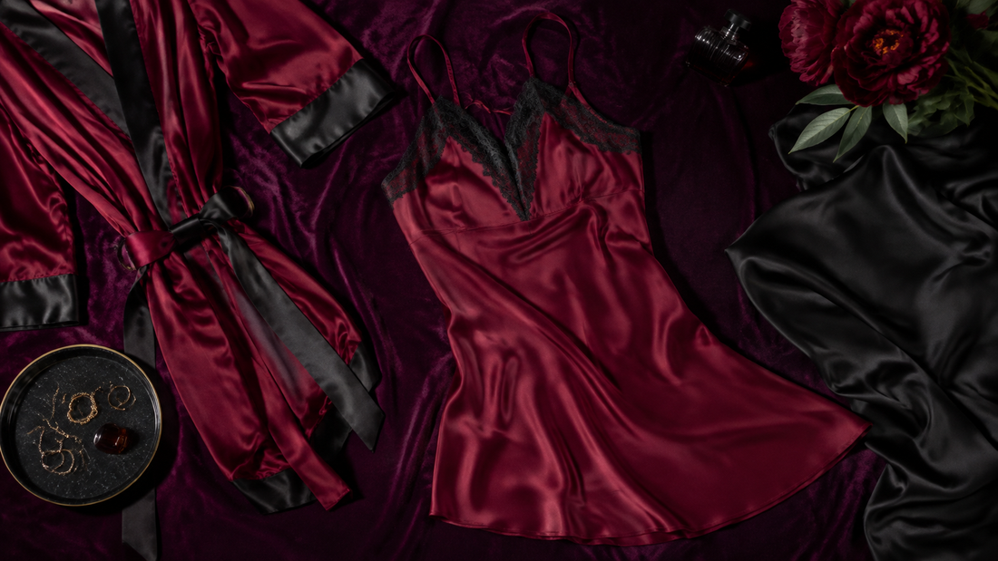 Burgundy satin camisole and matching robe arranged with black silk accents on plum velvet
