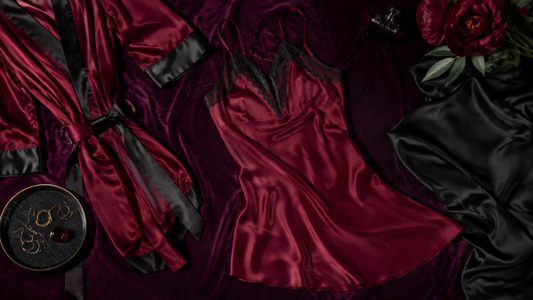 Burgundy satin camisole and matching robe arranged with black silk accents on plum velvet