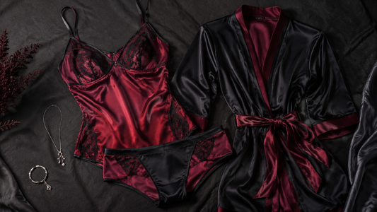 Deep red and black satin camisole, opaque brief and robe arranged on dark fabric