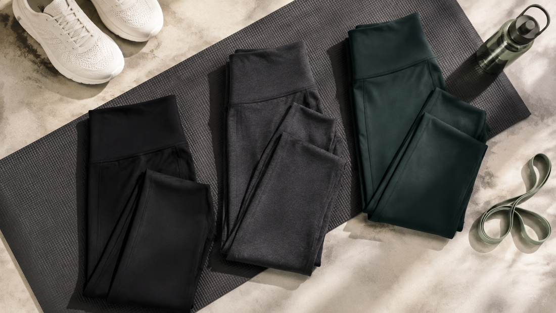 Black, charcoal and deep green leggings arranged with a yoga mat, sneakers and resistance band