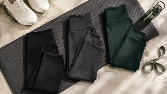 Black, charcoal and deep green leggings arranged with a yoga mat, sneakers and resistance band