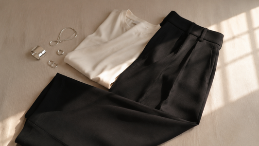 Black wide-leg trousers arranged with a cream top and minimal silver jewelry in soft window light