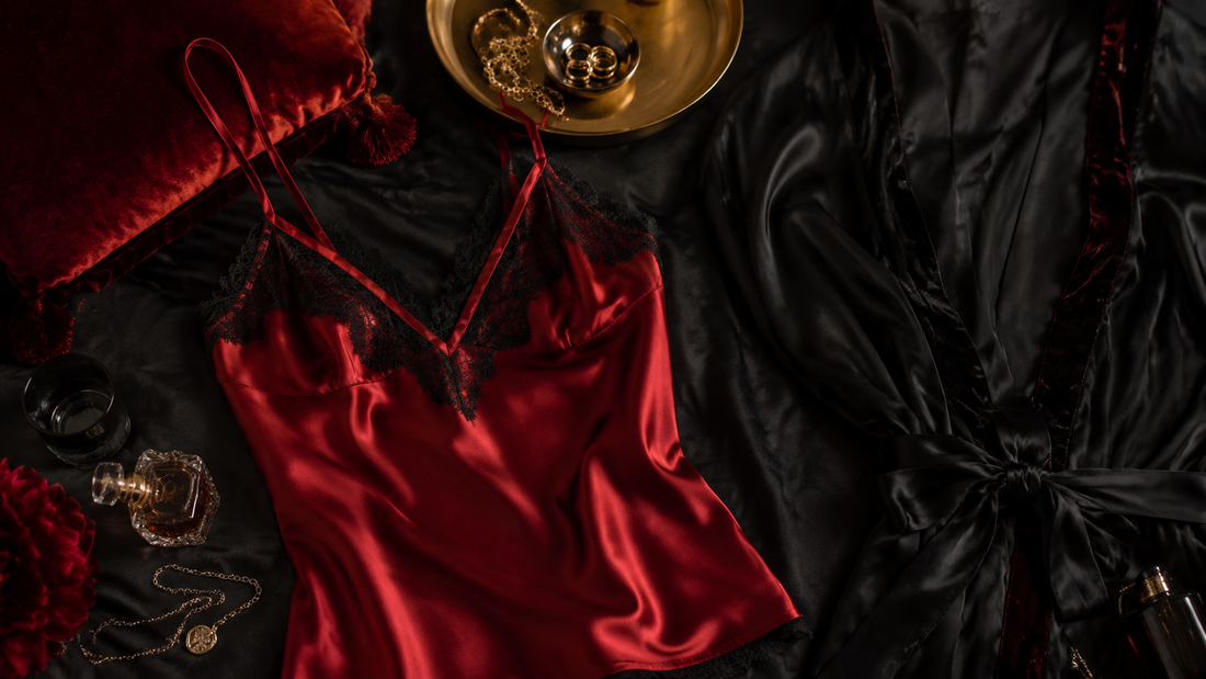 Deep red satin camisole and black silk robe arranged with muted gold accessories on dark fabric